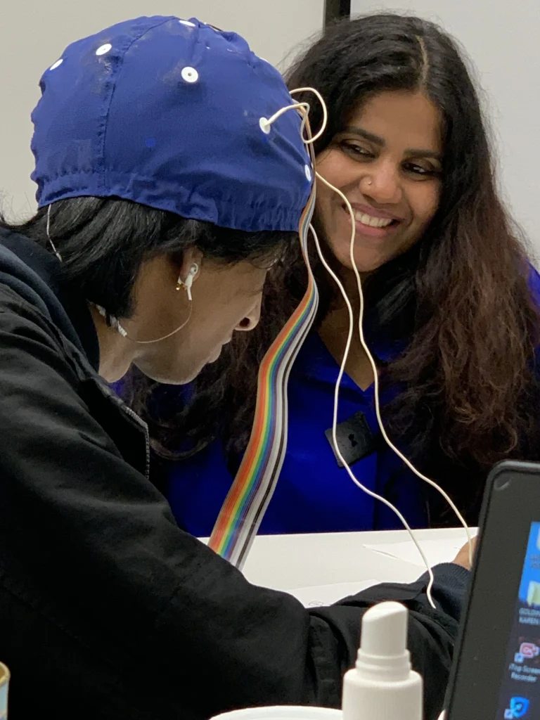 Kohila Sivas smiling beside a student wearing an EEG cap