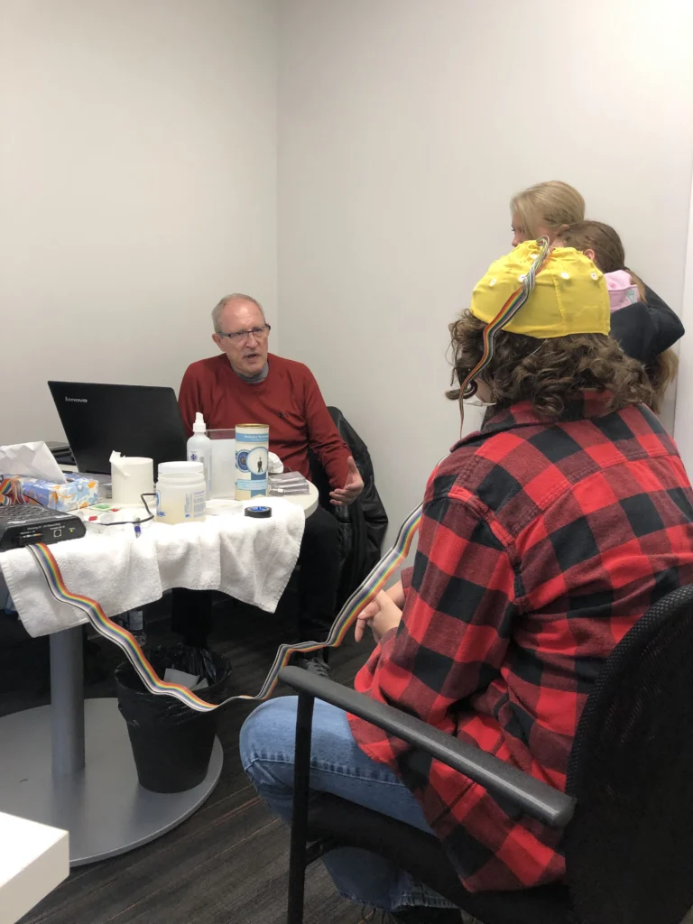 A child wearing an EEG cap during a session, with readings on a laptop nearby
